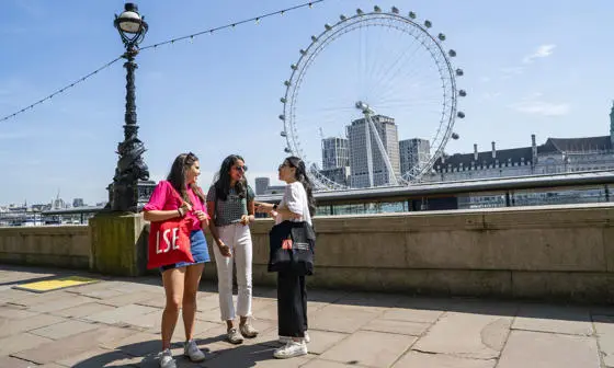 Three LSE students talking near the Thames with the London Eye in the background